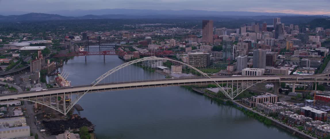 Drone view of an arch bridge over a river flowing through a city covering the landscape