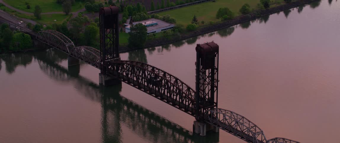 An aerial view of a bridge over a river ending on a margin with a garden