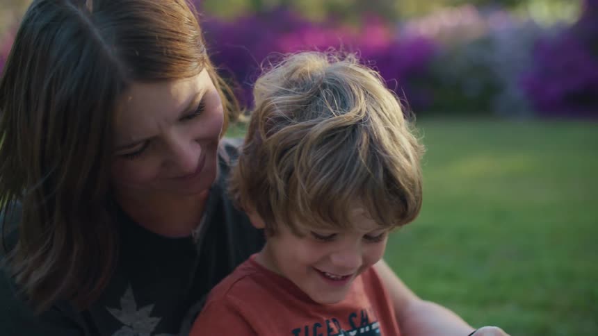 Woman sits with son on lawn and flips through book