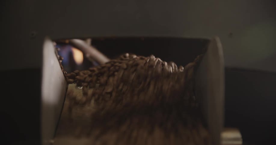 Person opens panel on coffee roasting machine to allow roasted beans to flow outward