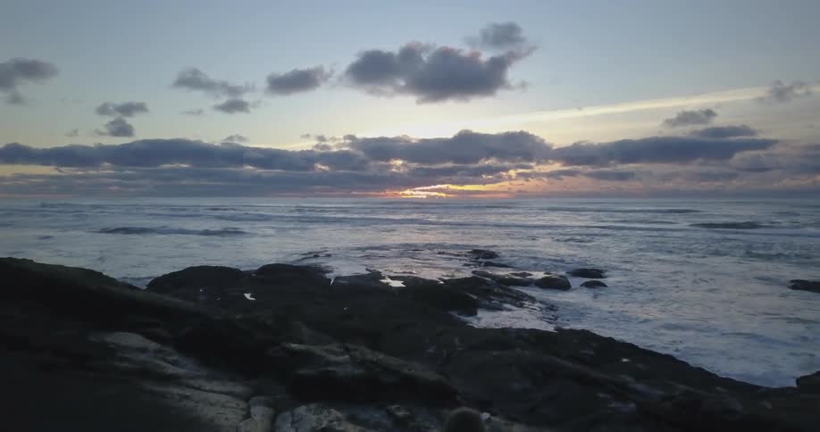 A person is sitting on a rocky outcropping at a beach at sunset