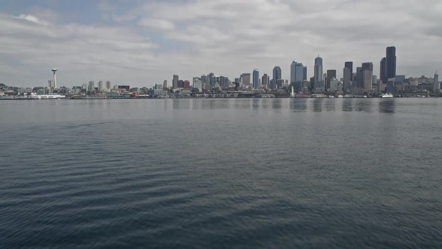 Aerial footage shows an approach approaching Elliot Bay from the water as the camera tilts up to reveal the Seattle skyline under cumulus clouds