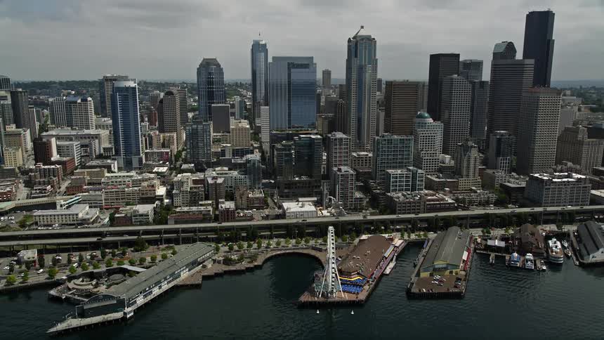 Approaching the Seattle skyline from the water the clip tilts down to showcase the iconic Great Wheel and bustling waterfront businesses below