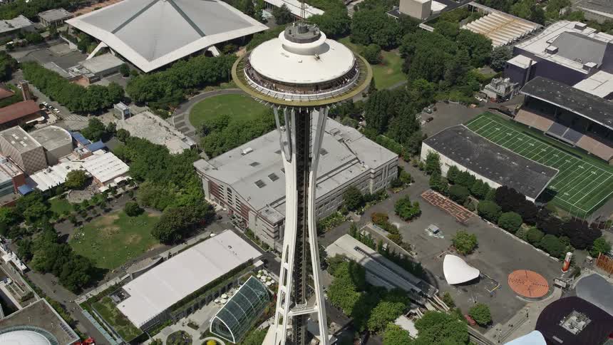 Approaching the iconic Space Needle flying over Downtown Seattle with a birds eye view and tilting down for a closer look at the landmark