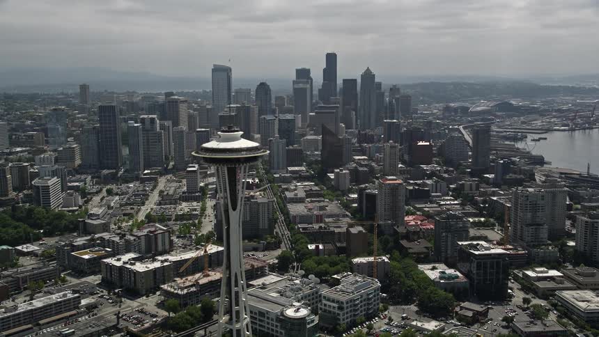 The aerial footage showcases the iconic Space Needle as the camera approaches Seattles bustling downtown skyline with partly cloudy skies