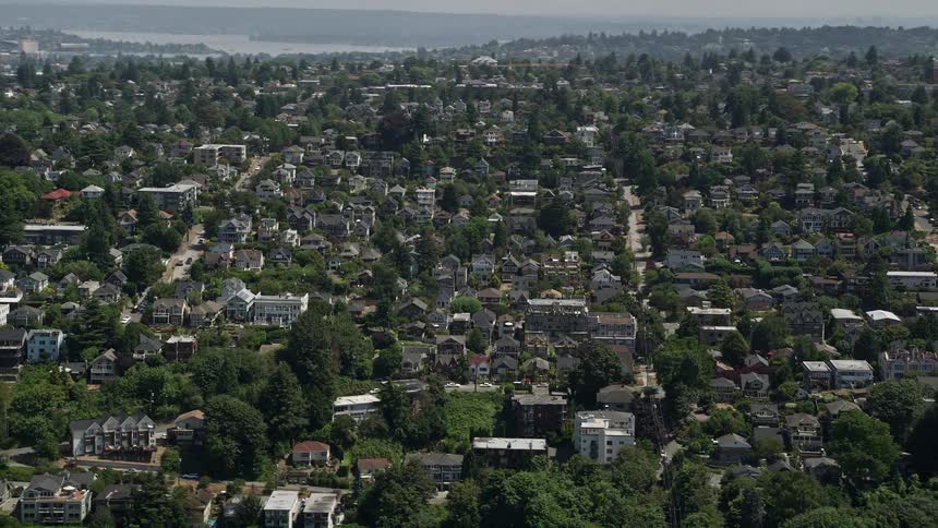 Flying over a sunny suburban neighborhood in Magnolia Seattle with close-knit houses and traffic on the streets during a hazy day
