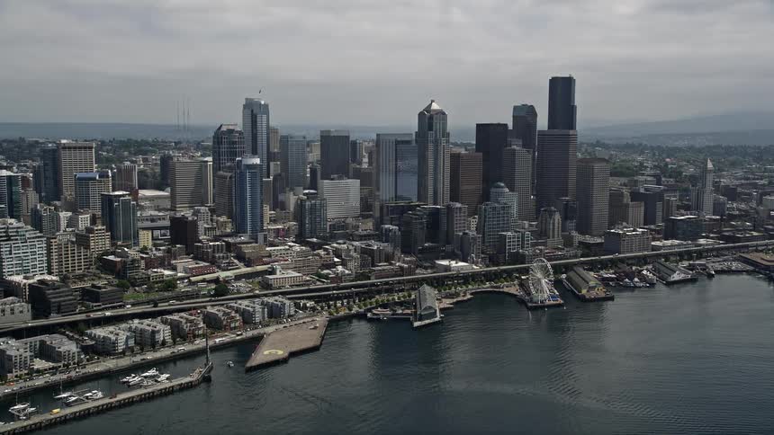 Approaching Seattles Waterfront and Downtown skyline from Elliot Bay showcasing the citys high-rises shoreline Ferris wheel and aquarium on a cloudy day