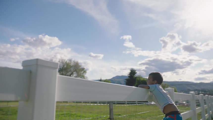 A white boy leans against a white fence outdoors