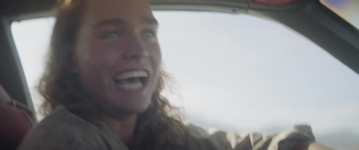 A woman smiles and shouts while driving a car