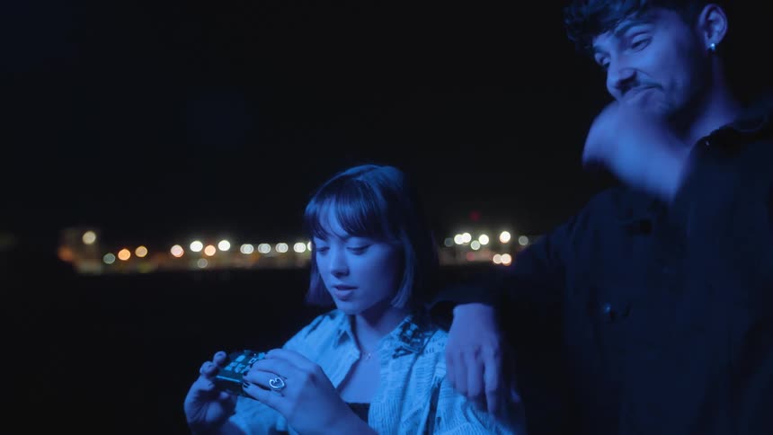 Woman takes selfie of herself and leaning man with camera at night