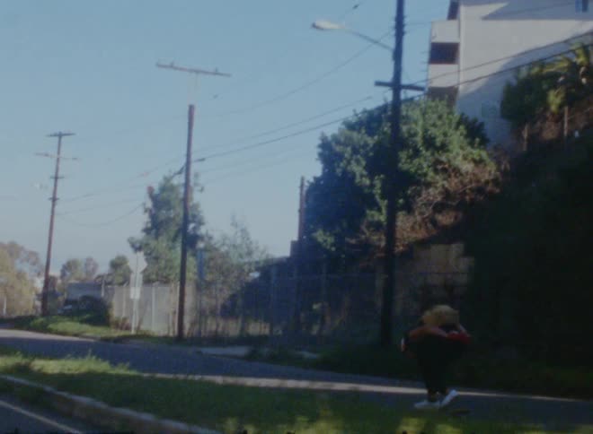 A teenage boy is wearing a backpack and riding a skateboard coasting on a neighborhood street
