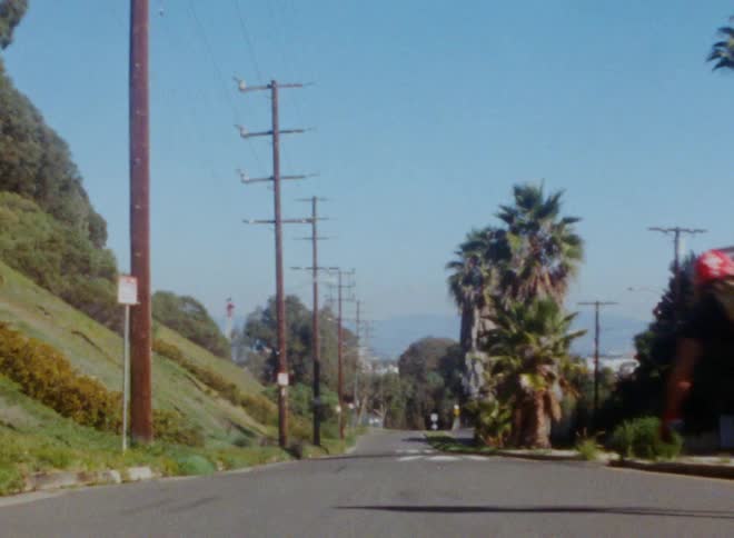 Male skateboarder rides skateboard down road at base of hill