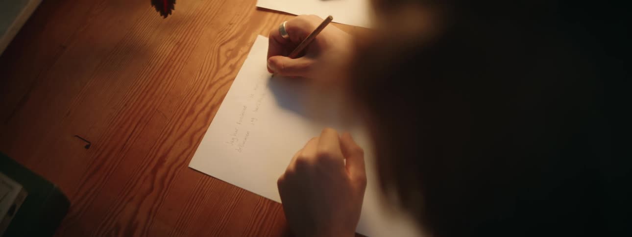 A person writing on a white piece of paper on a wooden desk