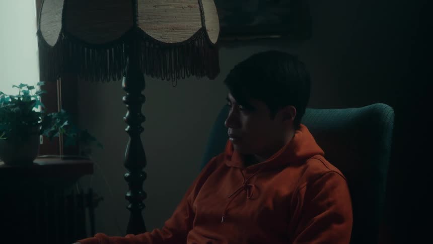 Light flickers in lamp before going out near man sitting in chair and wearing an orange hoodie