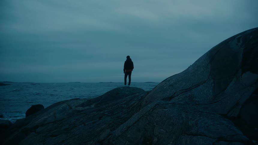 A person looks out over the ocean while standing atop a rock formation on the coast during the day