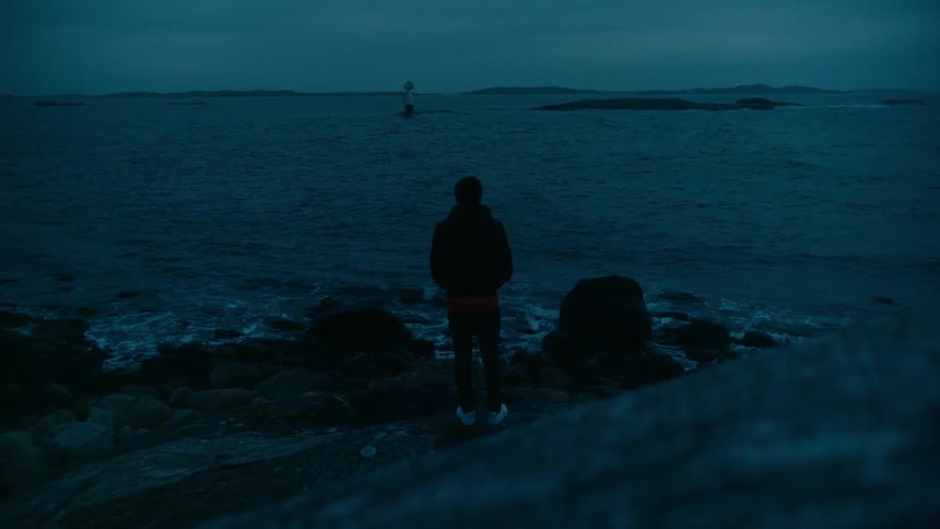 A man standing on rocks at the edge of a coastline as waves crash up against it
