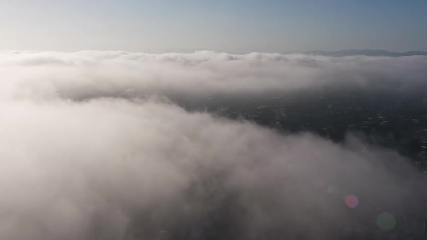 Beautiful 4K aerial view as camera tilts down from marine layer clouds revealing Los Angeles below on a cloudy day in Southern California