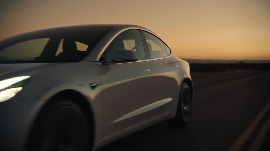 A white car speeding down a desert highway at dusk