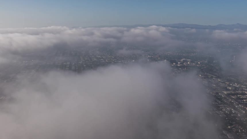 A 4K aerial shot of a break in the clouds hovering over a marine layer and Los Angeles