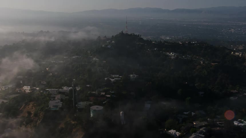 Aerial footage capturing the marine layer clouds gradually unveiling hillside homes and a radio tower in the upscale area of Beverly Hills California