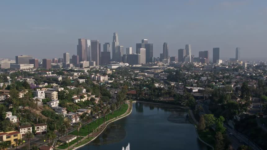 Fly over Echo Park Lakes fountain and approach Downtown LAs iconic skyline in this stunning 4K aerial footage captured over Californias metropolitan city during daytime