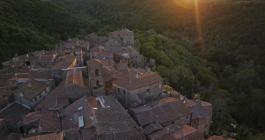 Sunlight glares onto forest surrounding historic town crowded together on hill
