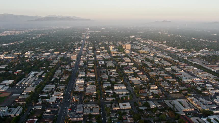 Aerial footage of urban neighborhoods in Van Nuys California during sunset with hazy sunset light and residential buildings