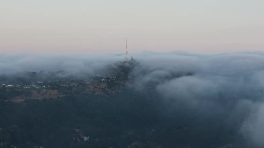 Aerial footage of a radio tower peeking through the marine layer during sunset over the Hollywood Hills in California