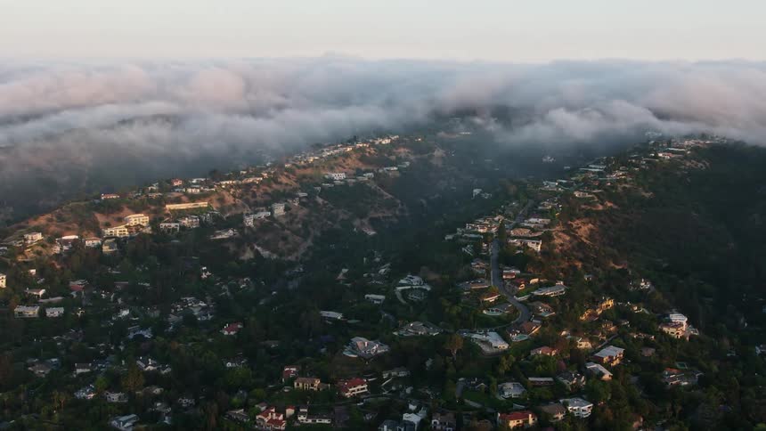 Flying over upscale hillside homes in Sherman Oaks California during dusk with fog rolling over the hills during a beautiful sunset