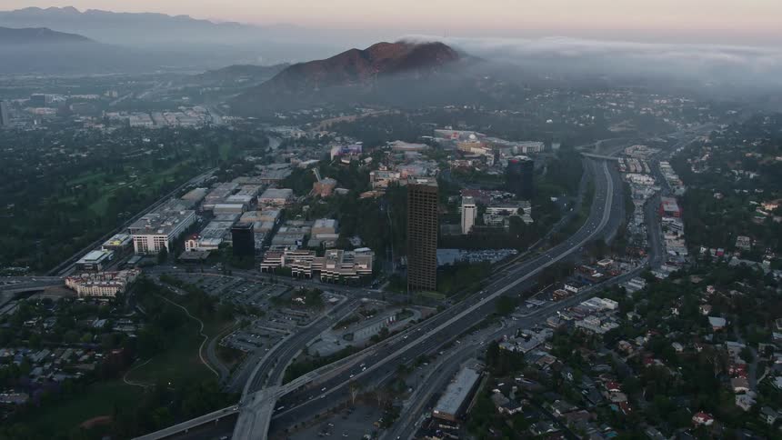 Aerial footage of fog rolling in near Universal City during sunset showing the city built around a fog-covered mountain in California