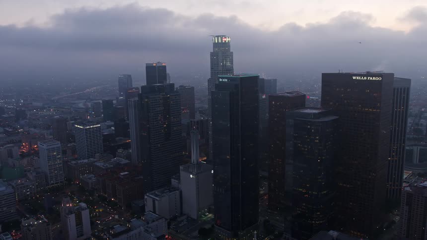 An aerial view of Downtown Los Angeles skyscrapers and high-rises orbiting under a marine layer during twilight