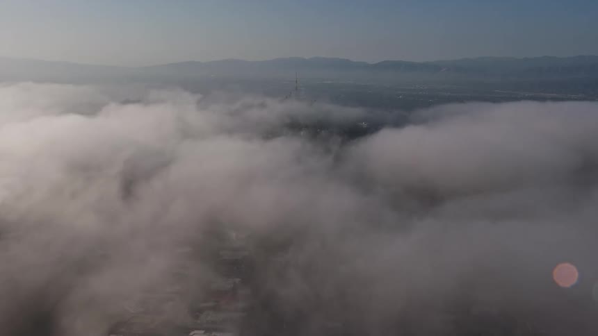 An aerial view of hillside homes and a radio tower in Beverly Hills California revealed through 4K footage flying over marine layer clouds