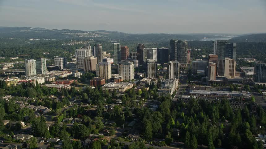 Aerial view of high rise buildings in Downtown Bellevue Washington with a sunny day and scenic backdrop of misty water