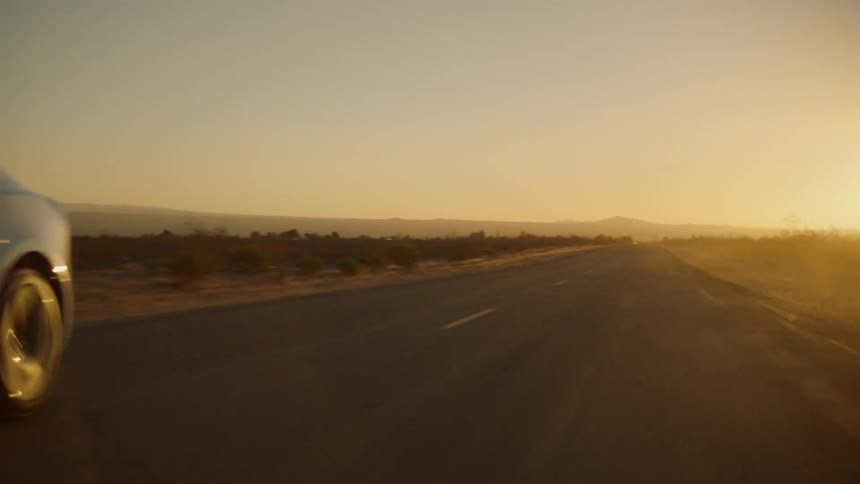Sun shines from just above horizon onto car driving along highway