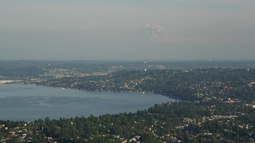 Aerial footage showcasing homes nestled in a suburban community surrounded by mountains and Lake Washington with Mount Rainier standing tall in the background on a sunny day in Seattle Washington
