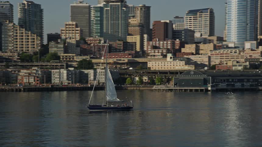 Aerial footage captures a sailboat raising sail on Elliott Bay revealing the waterfront and downtown Seattle Washington