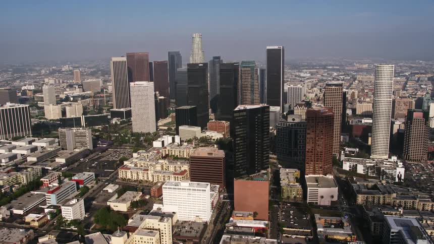 Aerial footage of Downtown Los Angeles skyscrapers towering over the cityscape on a hazy day shot from the north of the city