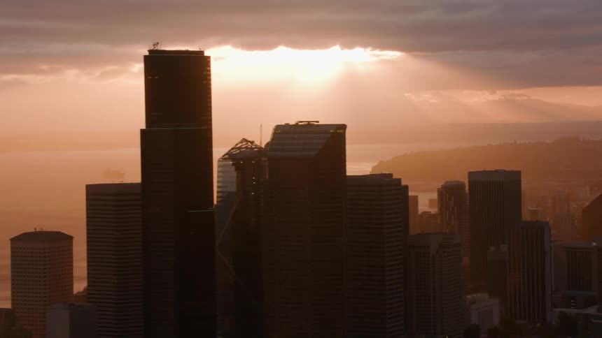 Sunlight shines through break in clouds turning fog red and casting coastal city buildings into partial silhouette