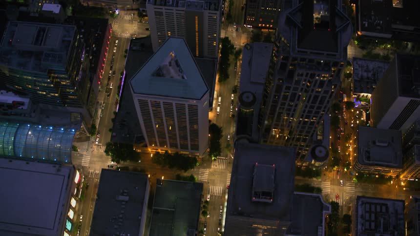 Traffic moves along city streets near a building with a glass ceiling at night