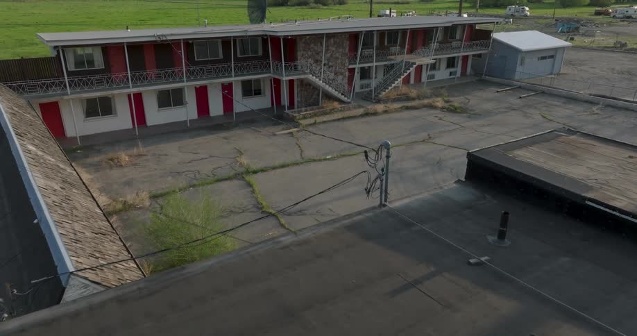 Weeds and tall grass grows between cracked pavement at a run down 70's motel