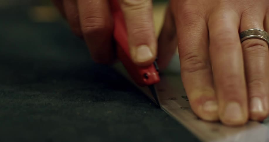 Seamstress cuts fabric on worktable using blade and ruler