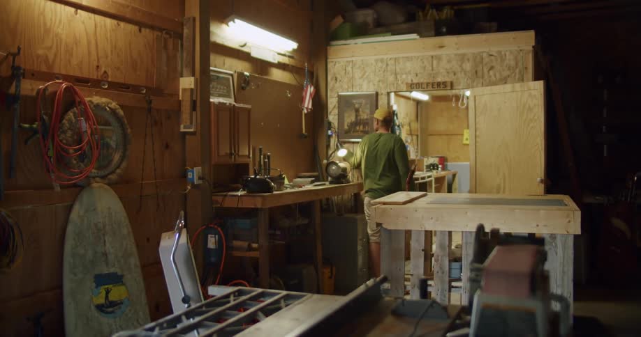 Man turns on light while walking through garage into enclosed room used as a workshop