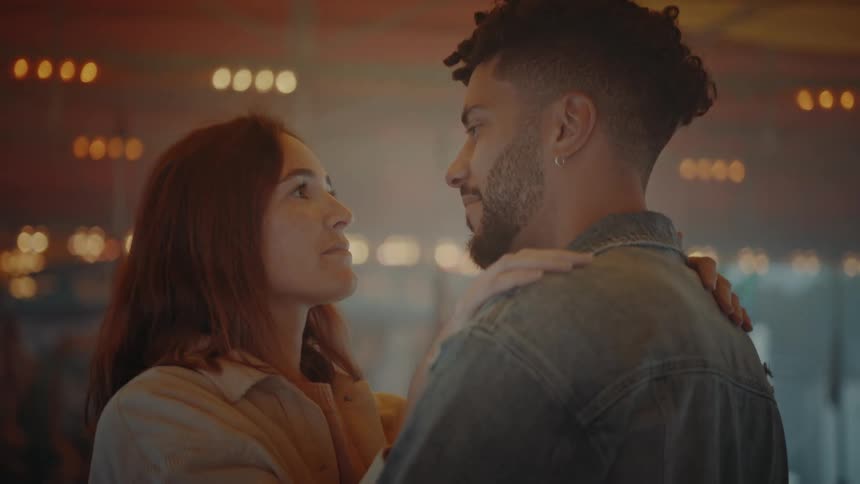 Man with beard earrings and denim jacket dances with woman with red hair and white shirt