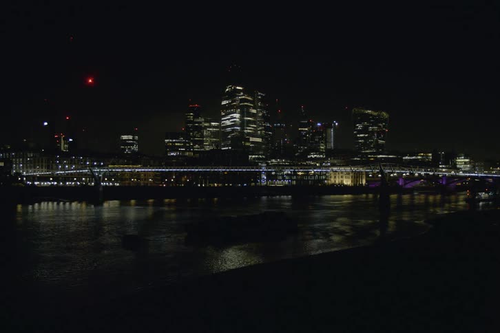 Wide shot of the city at night seen from the river bank with a bridge in between