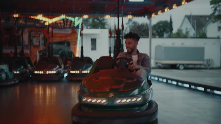 Brown man wearing denim and white redhead woman in a white coat drive around bumper cars