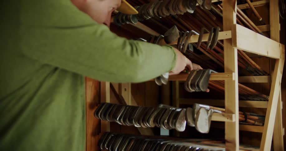 A man in a green shirt places golf clubs on a wooden rack