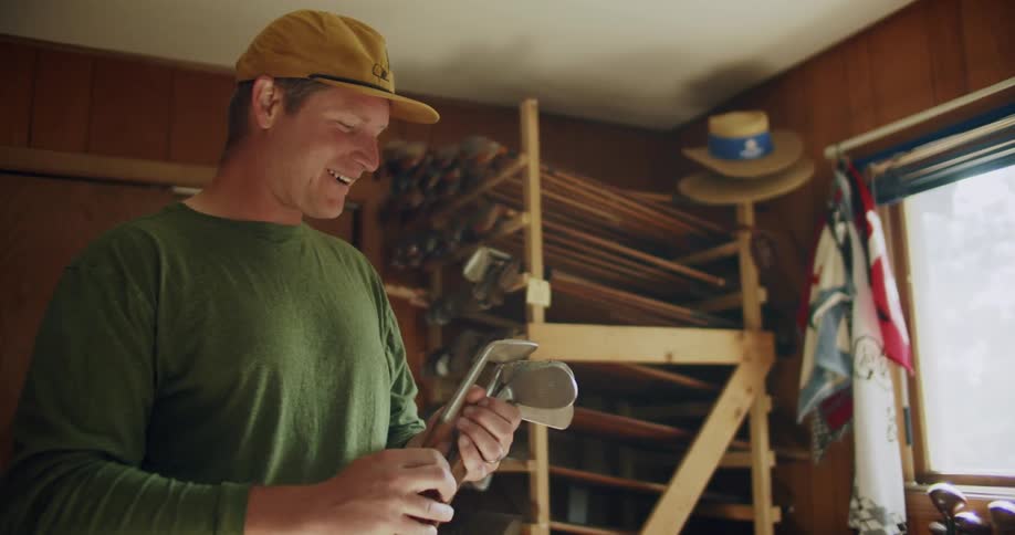 Man stands in room examining golf clubs near shelving holding multiple golf clubs