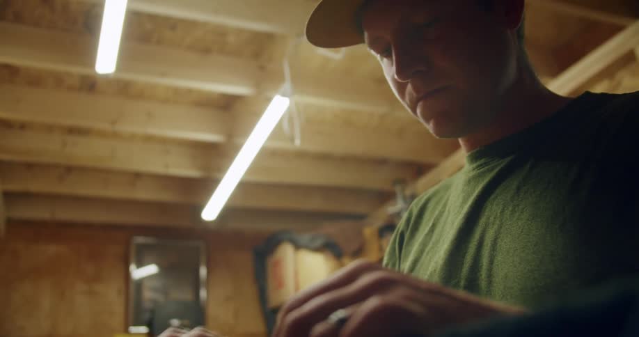 A man wearing a hat in a work shed hammers something