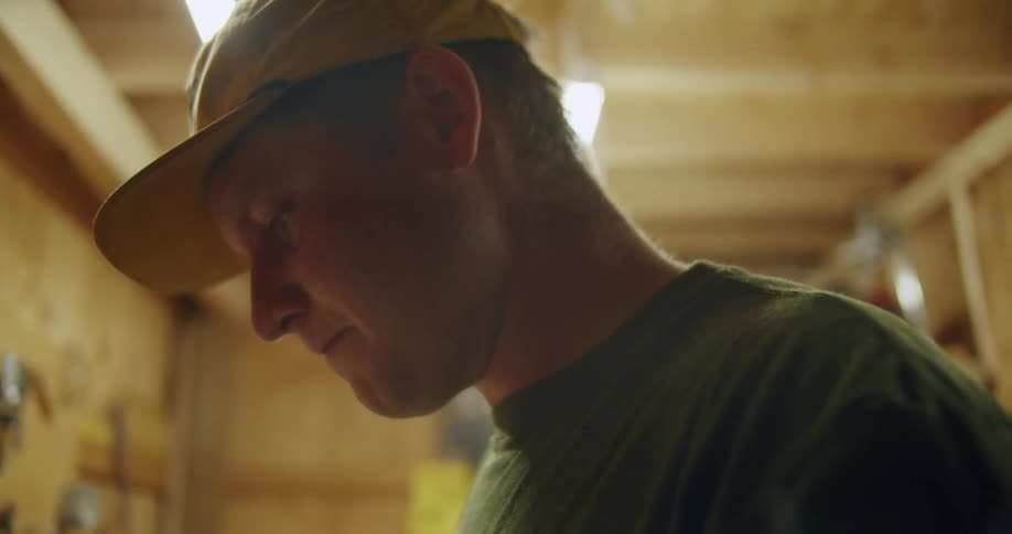 A man wearing a cap inside a warehouse looking down determined