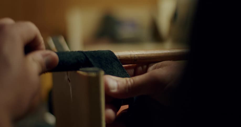 A man slowly wrapping fabric around wood to make a golf club